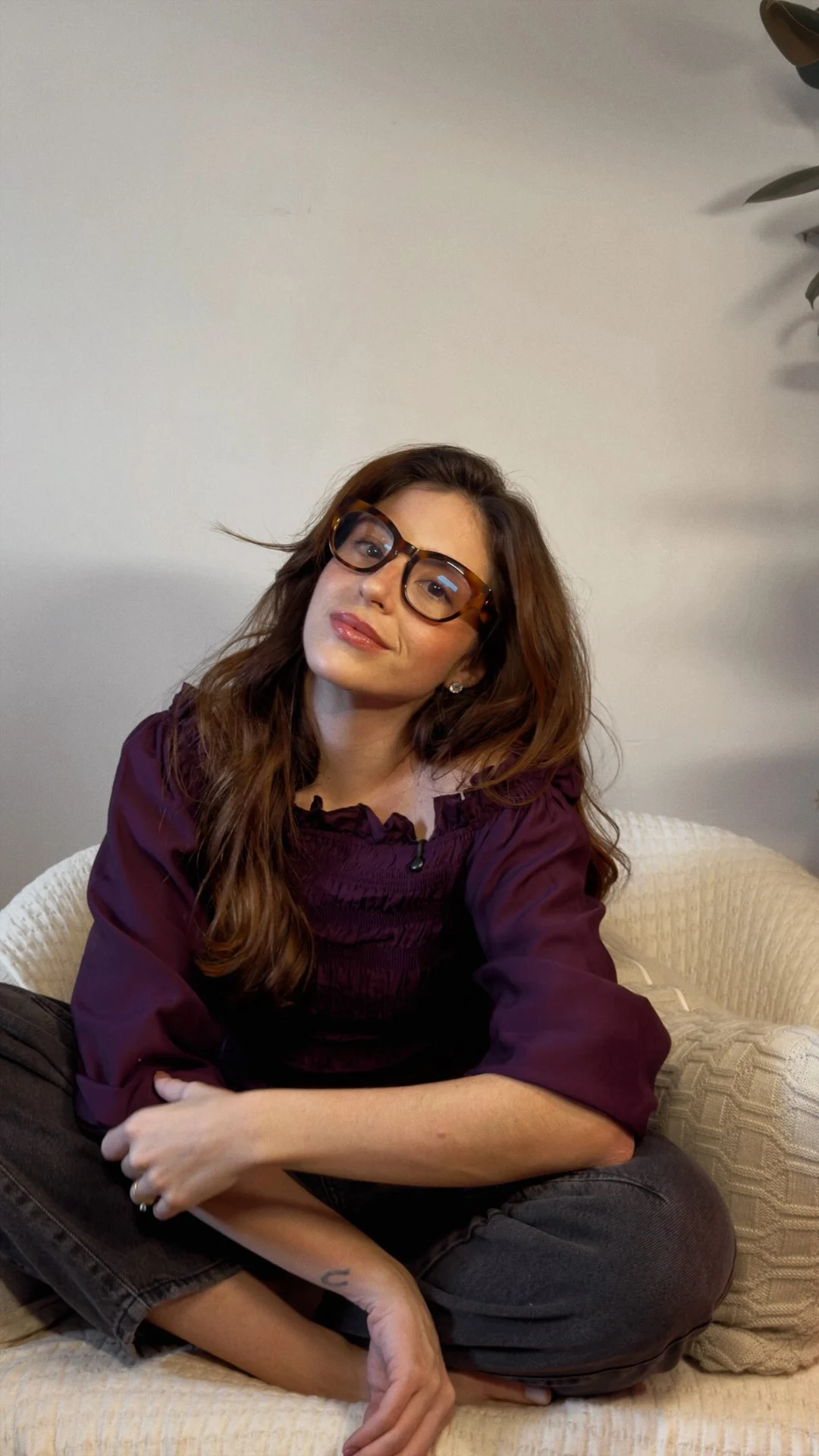 Rafaela sentada no sofá, usando óculos e camisa vinho