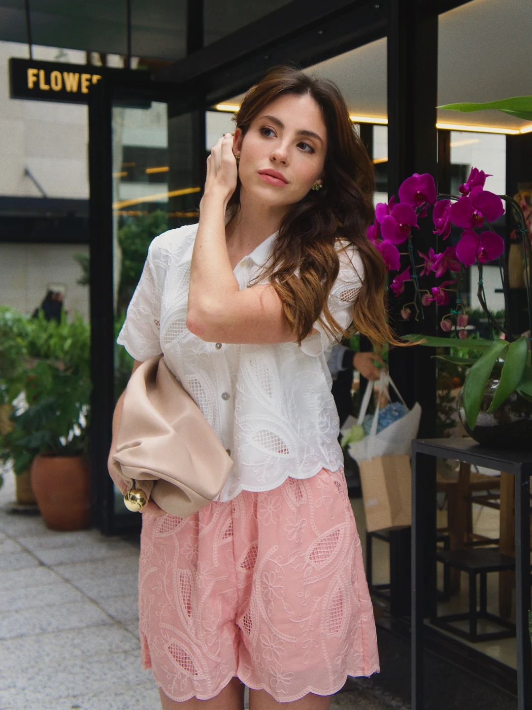 Rafaela de camisa clara e saia rosa diante de flores