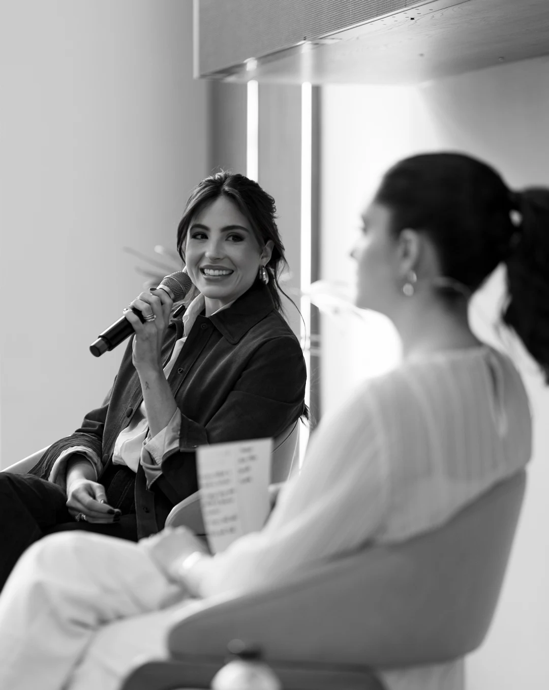 Rafaela sorrindo com microfone em um painel sobre marketing, em fotografia em preto e branco